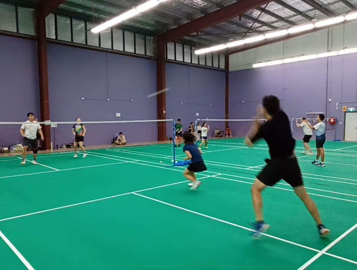 Players mid-game on the green courts at Vision Badminton Centre